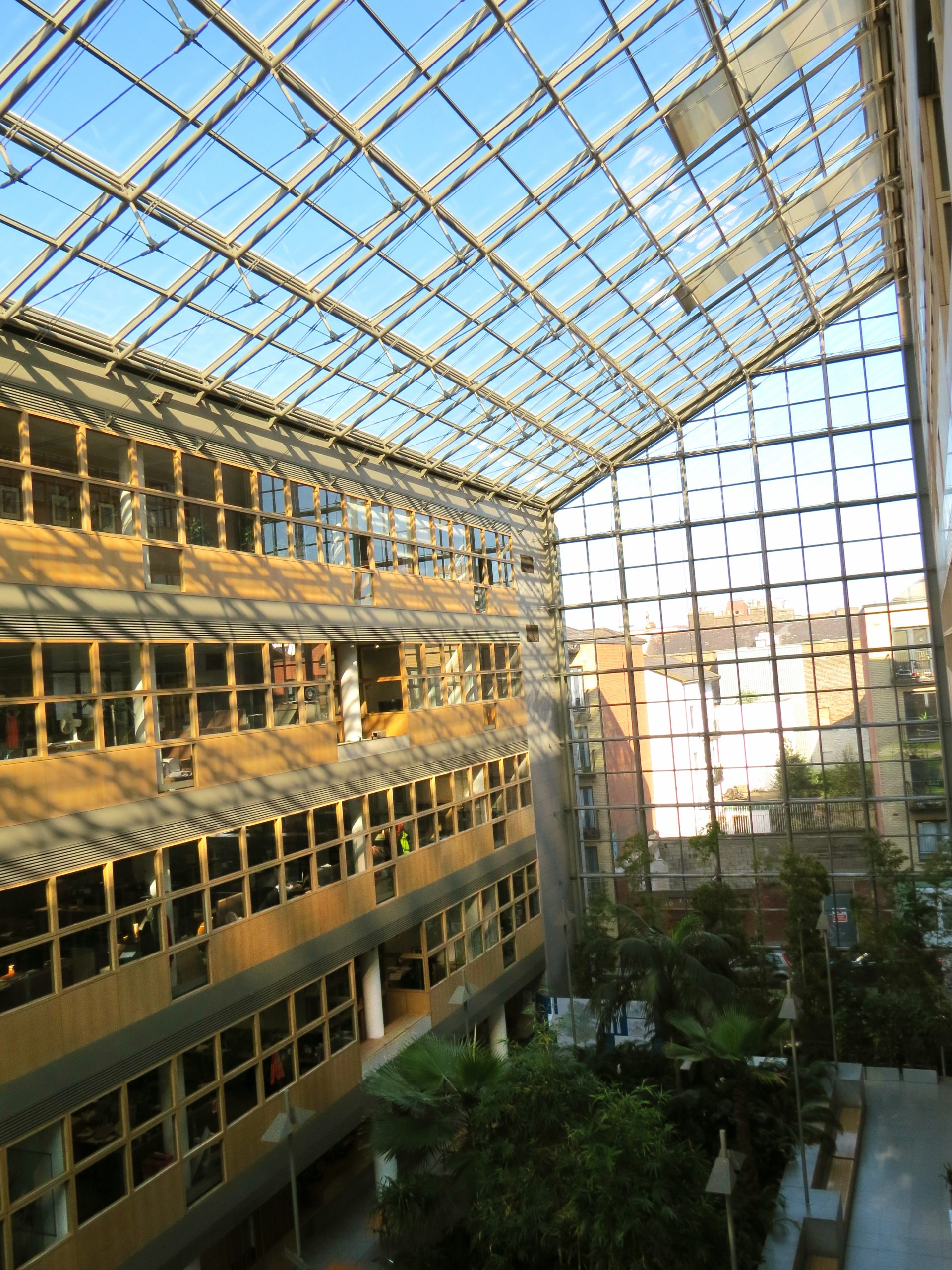 Internal picture of a 4-6 storey atrium with offices along the left hand wall with a cityscape visible through a glass wall