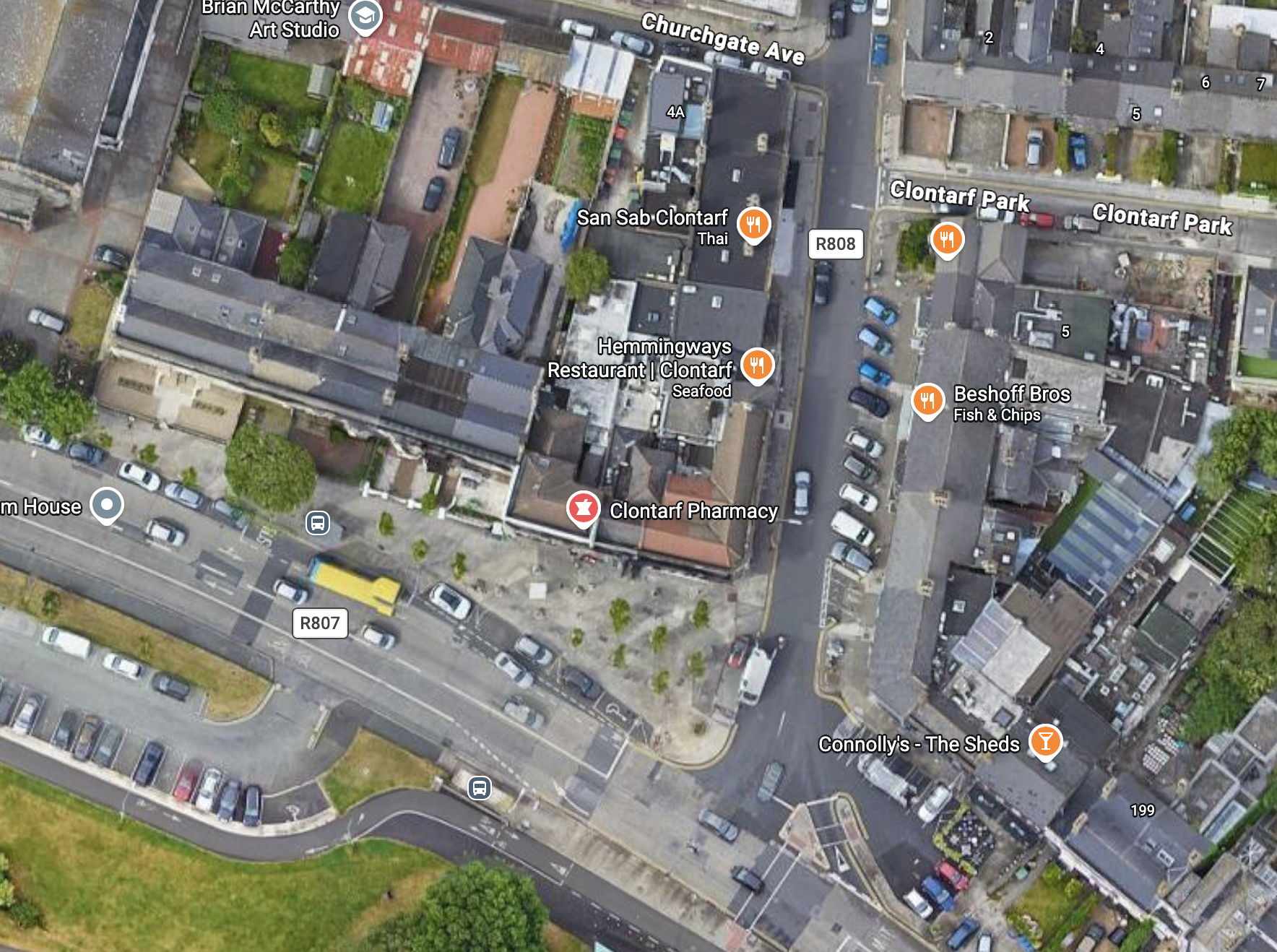 An aerial photograph of an urban/suburban neighbourhood with shops, car parking, trees and houses